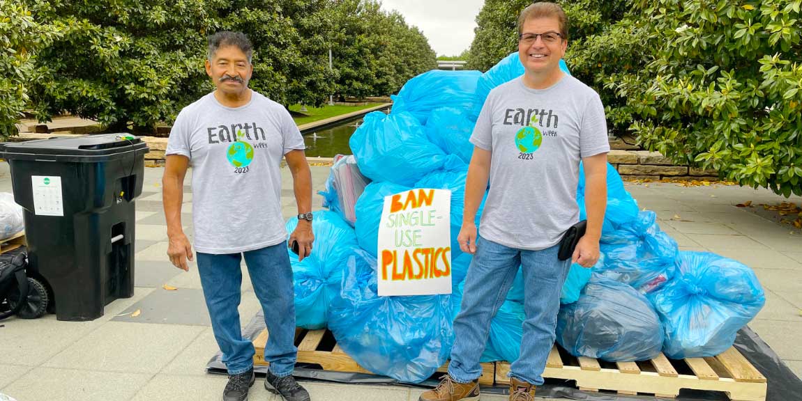 A pair of custodial workers in front of a large pile of filled plastic bags.